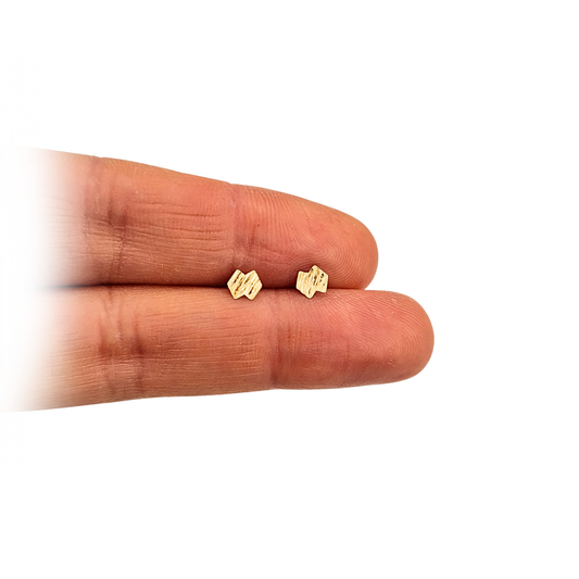 Pair of 9ct gold Brutalist stud earrings with textured abstract faces, each measuring 4mm wide. Unhallmarked but tested for purity, weighing 0.30g total. Fine minimalist design photographed on a model and shown against a measurement scale.