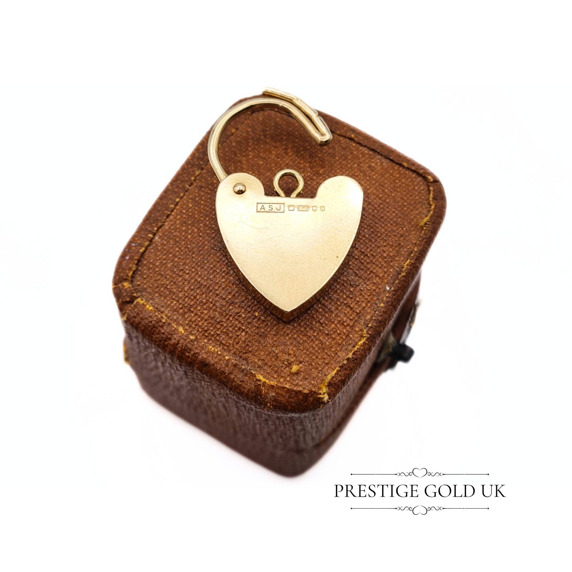 Close-up of a vintage 9ct gold heart-shaped padlock charm, featuring hallmarks from London, 1975, displayed on a vintage brown jewellery box.