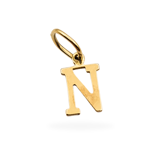 Tiny 9ct solid gold letter N pendant, measuring 10mm tall and 5mm wide with worn but tested hallmarks, shown against a scale and held for size reference. Dainty serif-style initial charm ideal for necklaces or bracelets, weighing 0.29g.
