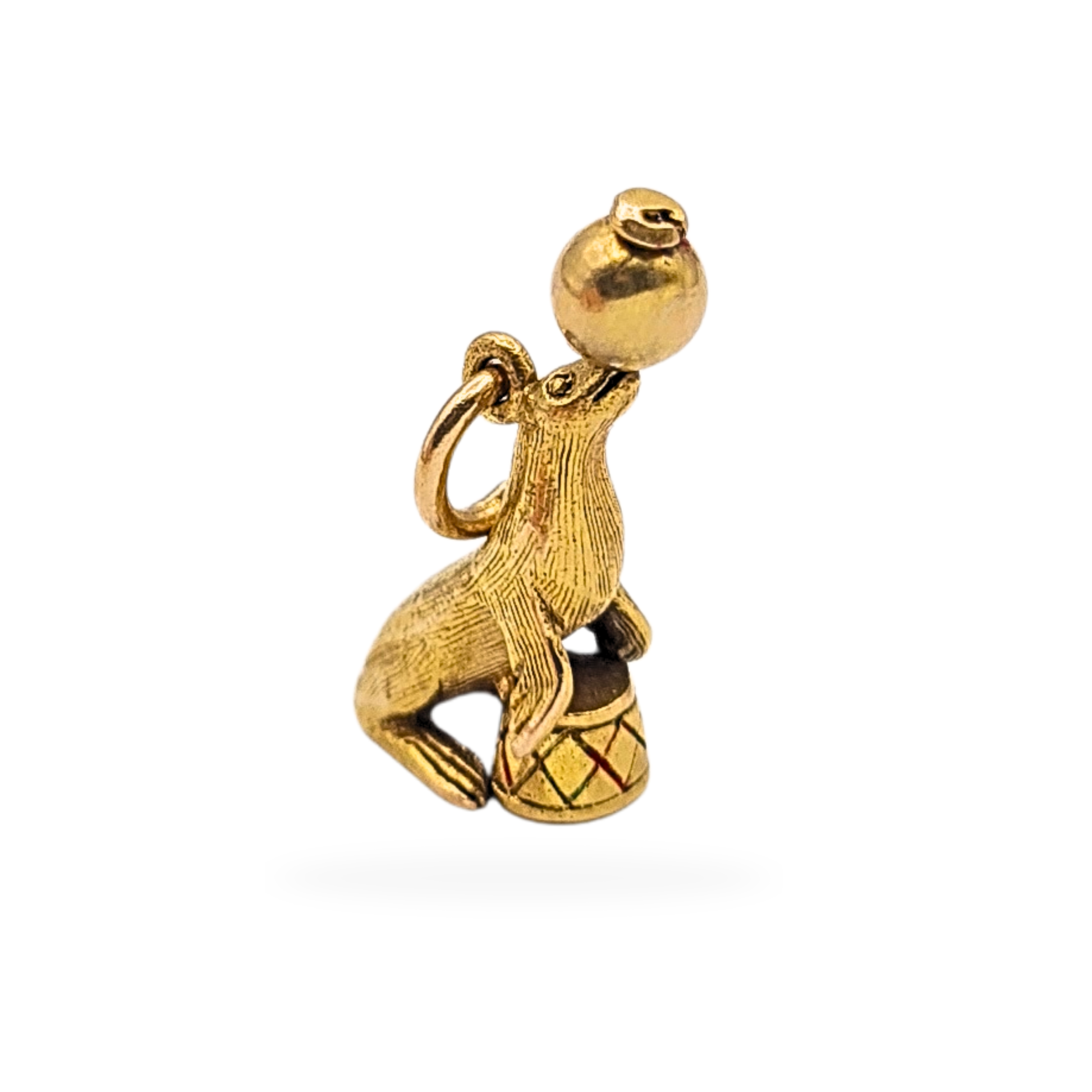 9ct gold circus seal charm pendant, fully hallmarked at Birmingham, 18mm tall and weighing 1.9g, featuring a detailed seal balancing a polished gold ball on an enamelled drum base. Textured finish with traditional British assay marks, good pre-owned condition.

