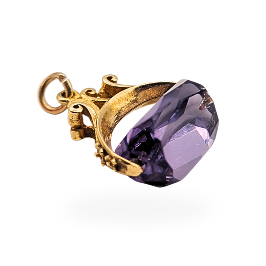 Vintage 9ct gold spinning fob pendant set with a faceted purple amethyst gemstone, fully hallmarked London 1969. Ornate scrollwork mount with swivel rotating stone, measuring approximately 17mm wide and 18mm tall, shown beside ruler and on fingertip for scale.