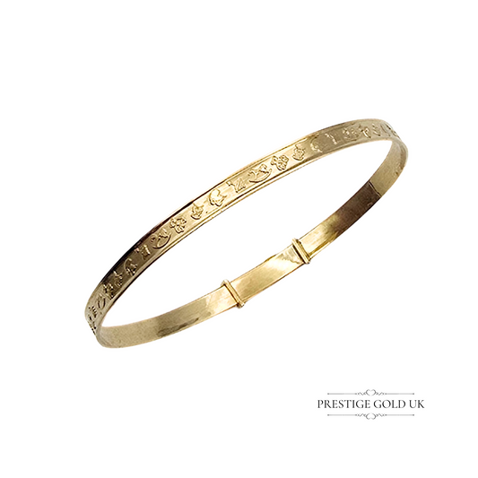A delicate 9ct gold baby bangle resting on a vintage red jewellery box, showcasing its intricate embossed design.