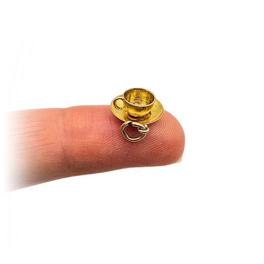 Tiny 9ct gold teacup and saucer charm measuring 11mm wide and 4.5mm tall, weighing 0.62g. Stamped 9ct and fully tested, featuring a miniature cup with handle on matching saucer, ideal for a charm bracelet or delicate gold necklace.
