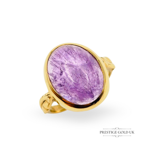 A stunning 9ct gold ring featuring a vibrant purple cabochon-cut suspect agate stone, bezel set in a smooth polished frame with elegant leaf-motif shoulders. Hallmarked in Birmingham, this unique ring is a UK size L 1/2. A one-off item, only one available—crafted with charm and sophistication.