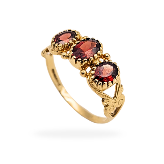 Vintage 9ct gold three stone garnet ring featuring oval-cut deep red garnets in an ornate heart-detail setting. Fully British hallmarked 375 gold, UK size O / US size 7 1/2, weighing 2.1g, with light age wear consistent with careful vintage use.