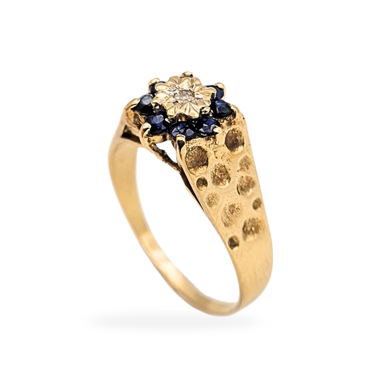 Vintage 9ct yellow gold flower cluster ring set with a central diamond and surrounding blue sapphires, featuring a dimpled textured band. Fully hallmarked London 1972, sized UK Q US 8, with a raised floral head measuring 9mm wide.